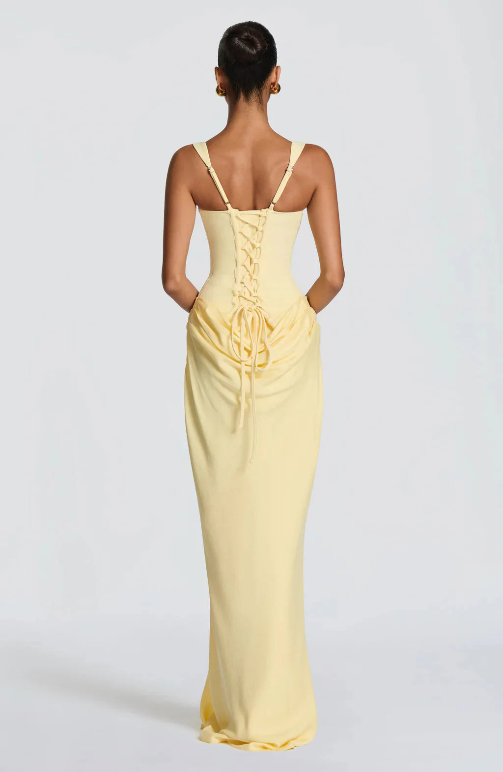 Back view of a light yellow Celeste corset maxi dress showing the lace-up corset detail and draped skirt.