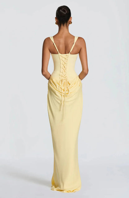 Back view of a light yellow Celeste corset maxi dress showing the lace-up corset detail and draped skirt.