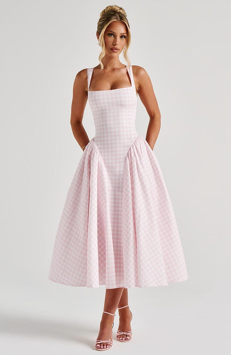 Full-length view of a pink gingham corset midi dress with wide straps and a full pleated skirt, paired with pink heels.