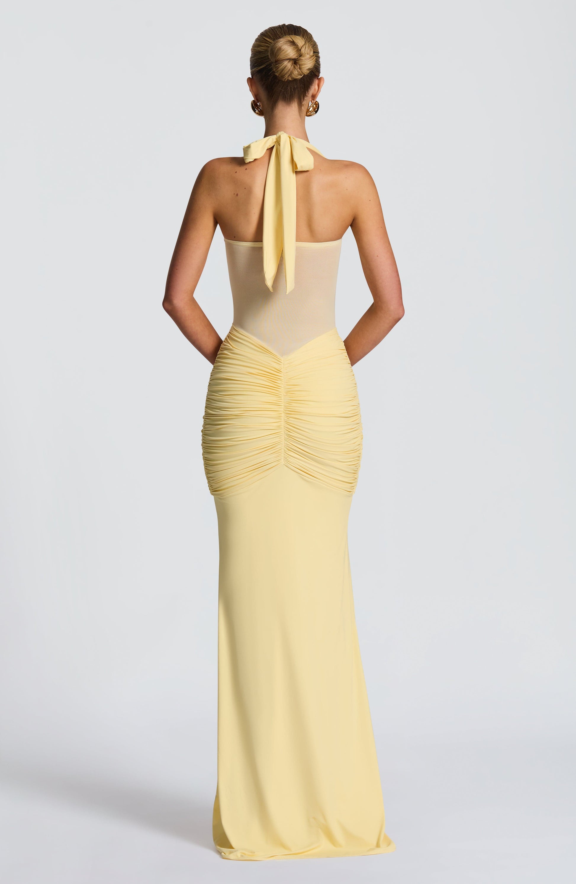 Back view of the light yellow Jayleen Ruched Maxi Dress, featuring a tie-back halter and ruched detailing.