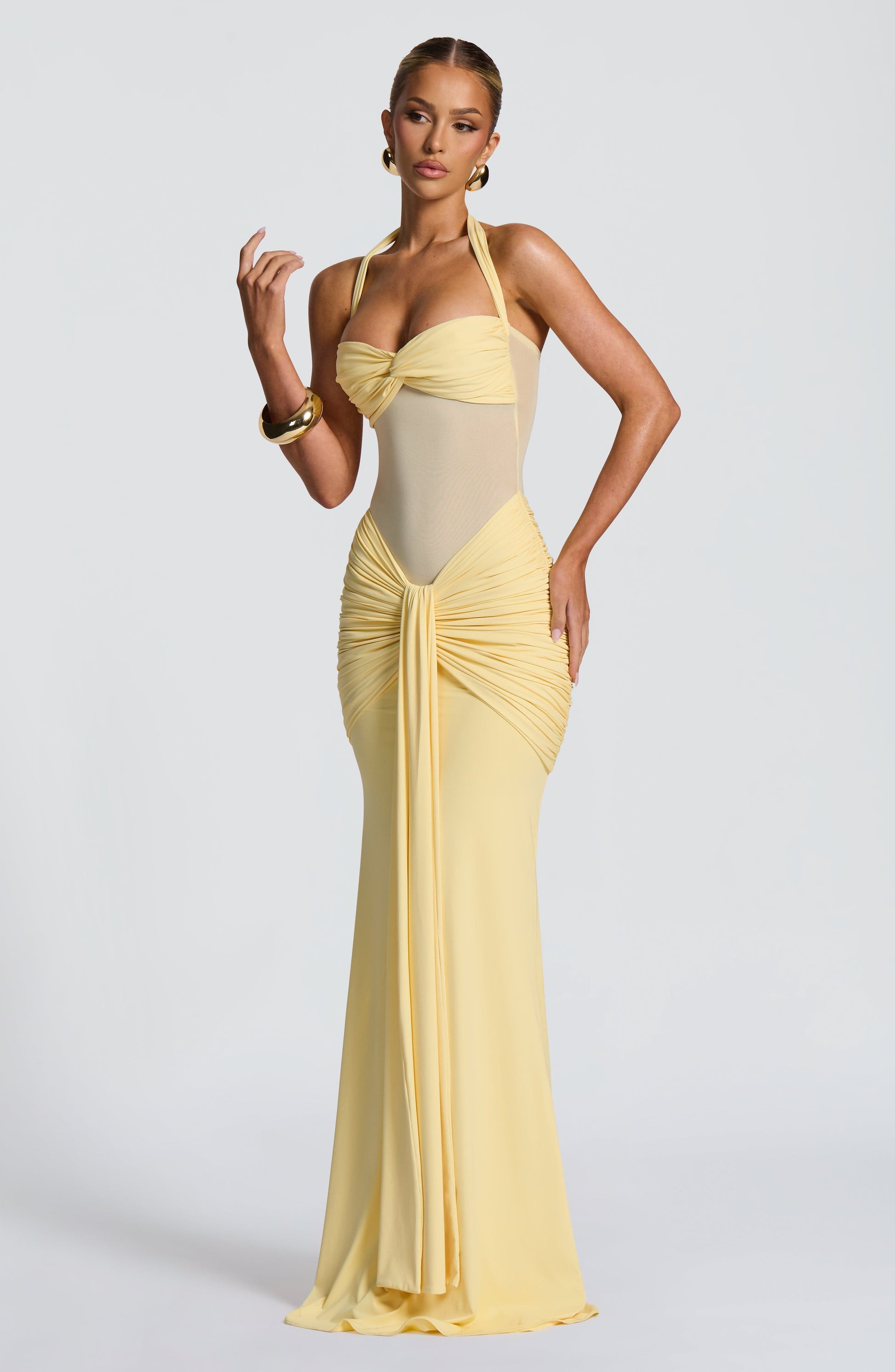 Side profile of the light yellow Jayleen Ruched Maxi Dress with a halter neck and draped skirt.