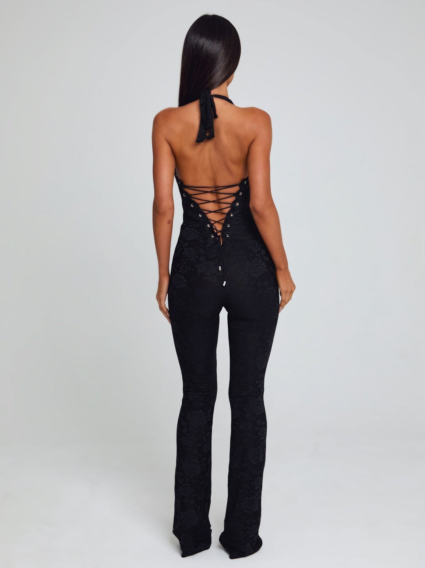 Rear view of a black Kenzie Halter Jumpsuit, featuring a lace-up corset-style back and floral lace texture.