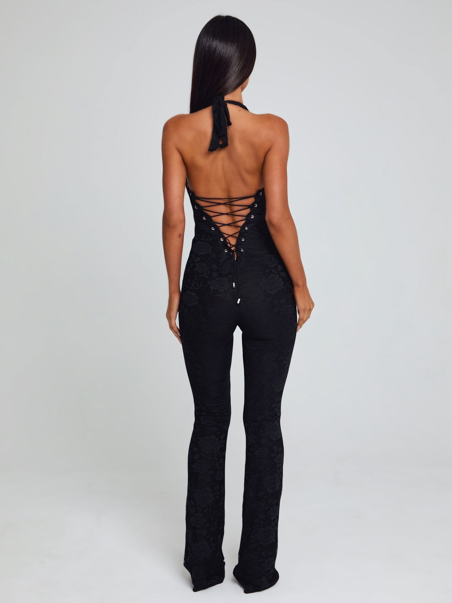Rear view of a black Kenzie Halter Jumpsuit, featuring a lace-up corset-style back and floral lace texture.