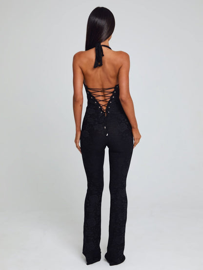 Rear view of a black Kenzie Halter Jumpsuit, featuring a lace-up corset-style back and floral lace texture.