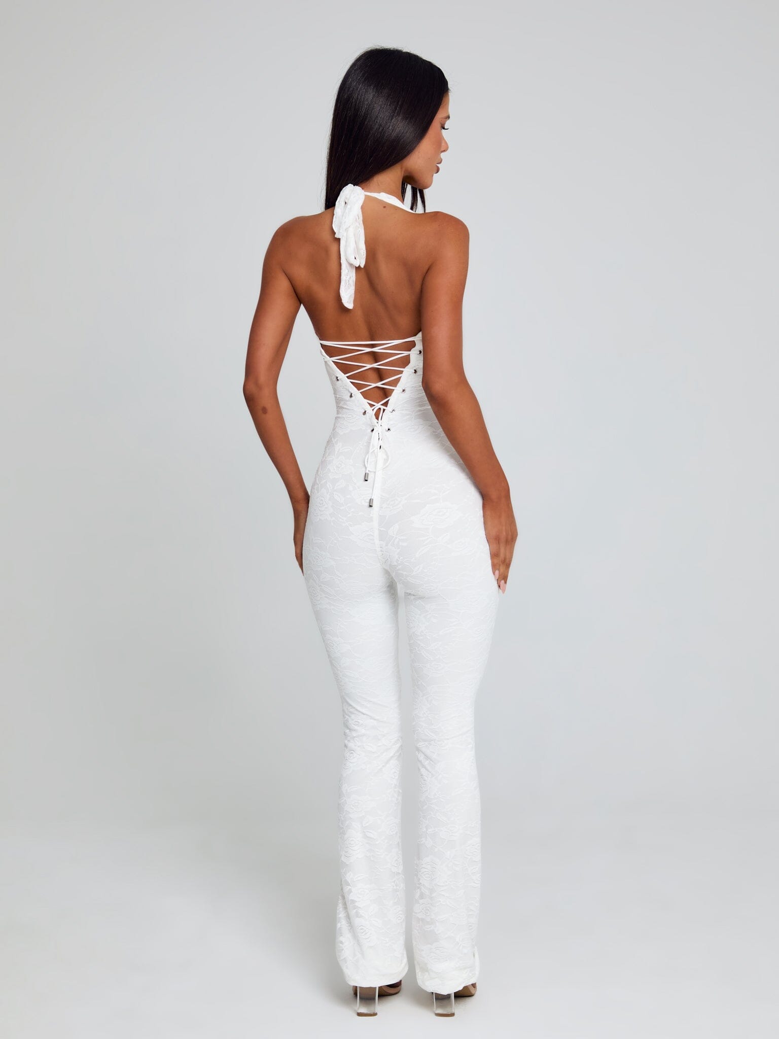 Back view of a white Kenzie Halter Jumpsuit, highlighting the white lace-up corset detail and floral lace fabric.