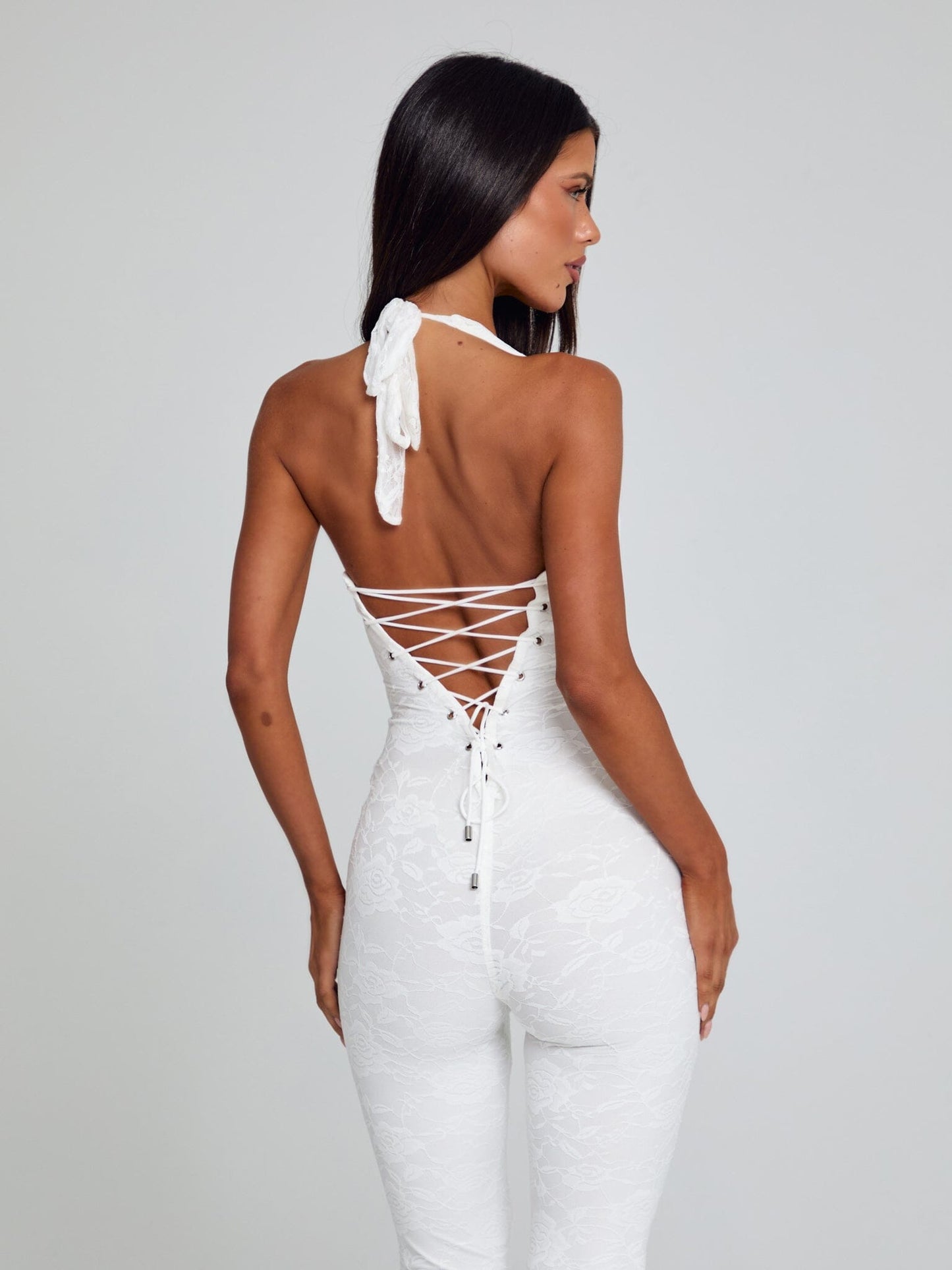 Angled rear view of a white Kenzie Halter Jumpsuit, showing the halter neck tie and intricate back lacing.