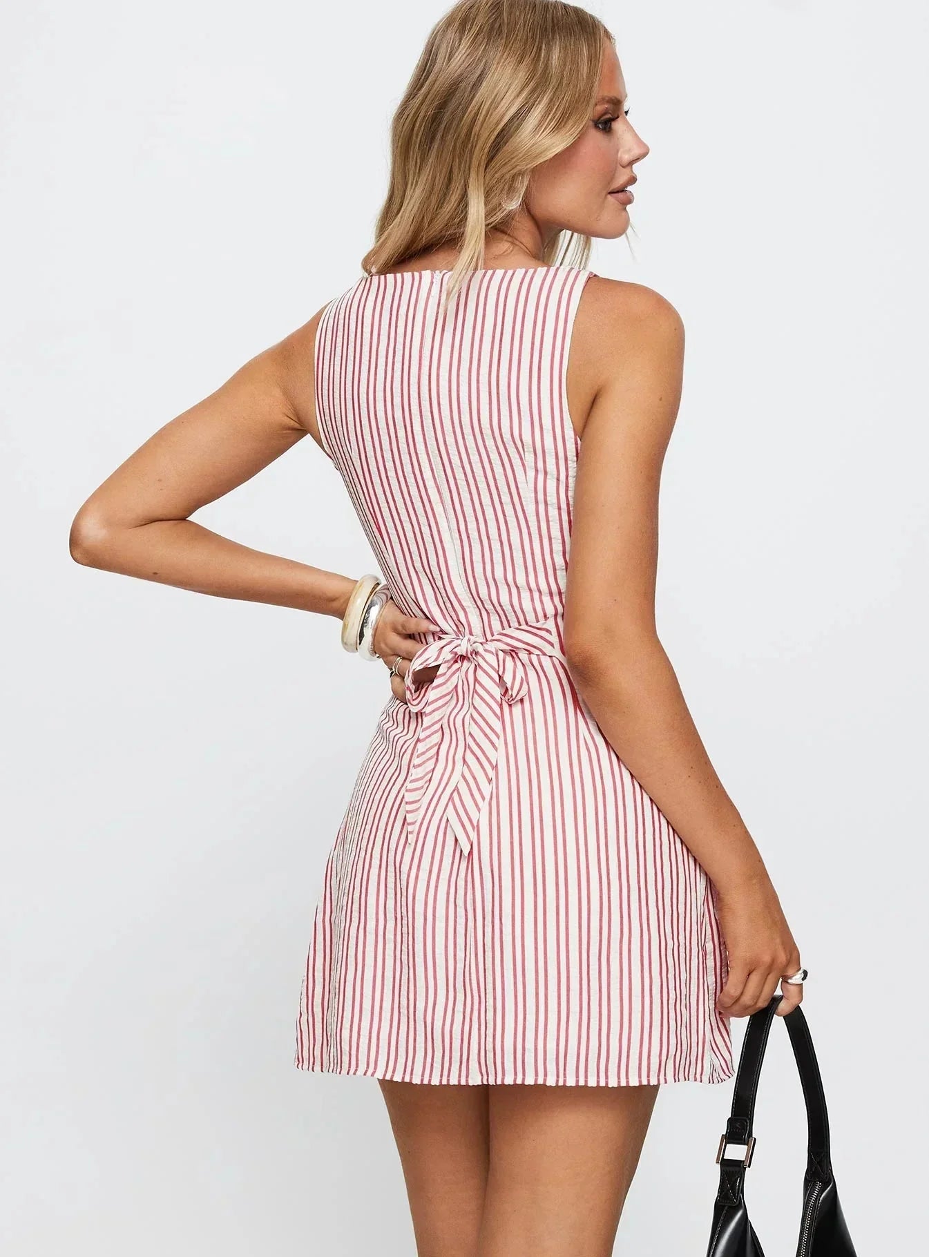 Back view of a sleeveless Lauren striped mini dress with red vertical stripes and a tied bow at the waist.