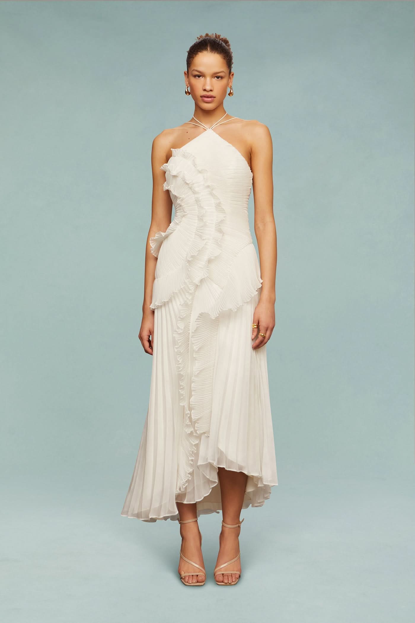 Model standing in a white Millie Ruffle Midi Dress, featuring a pleated skirt and distinctive ruffled design.