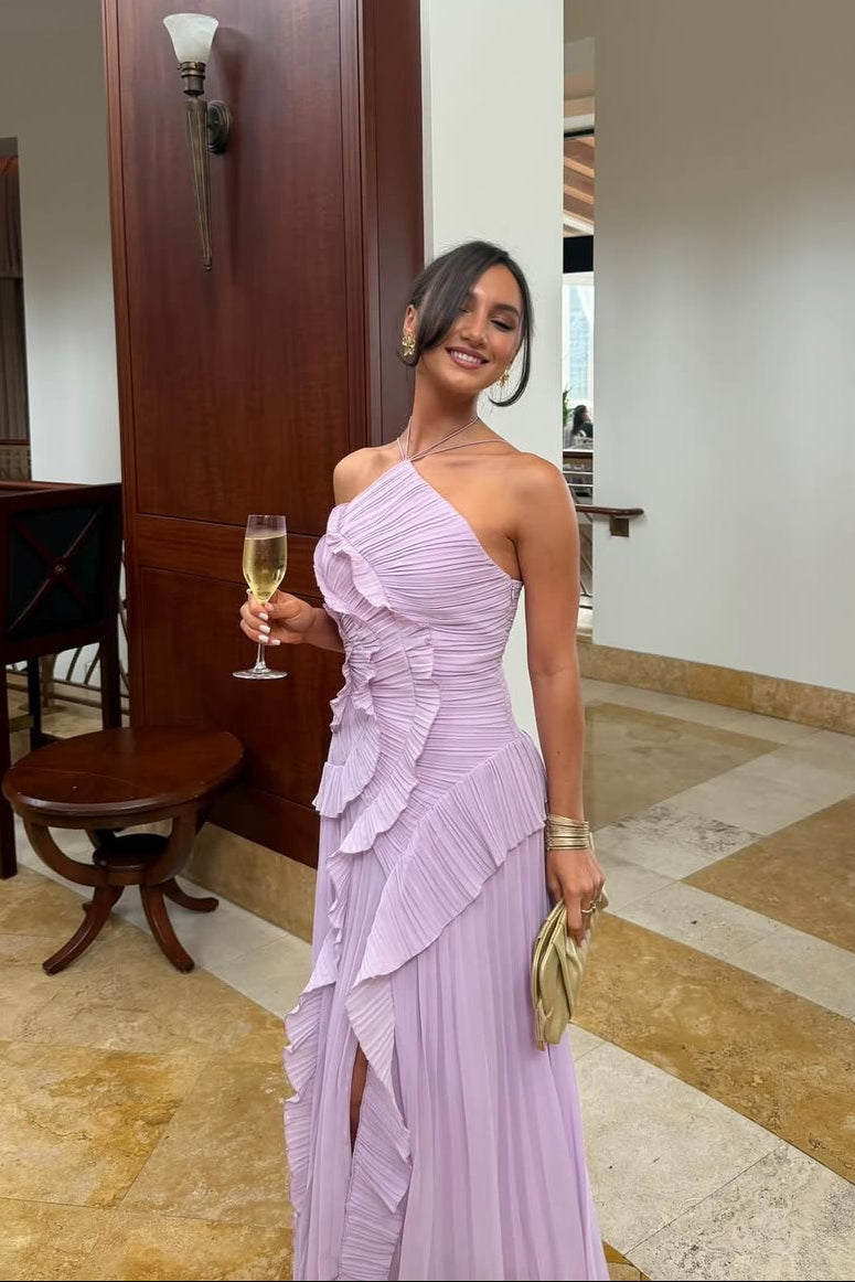 Woman in a lilac Millie Ruffle Midi Dress with a high slit and one-shoulder design, holding a glass of champagne in an indoor setting.