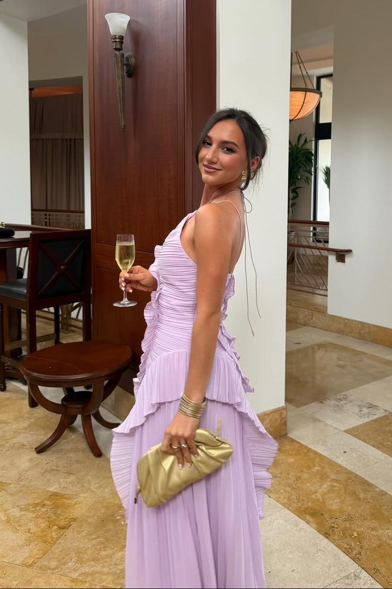 Side profile of a woman wearing the purple Millie Ruffle Midi Dress, showcasing the pleated skirt and gold clutch accessory.