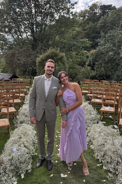 Couple posing outdoors, woman wearing the lavender Millie Ruffle Midi Dress with a pleated skirt and halter neck, man in a tailored suit.