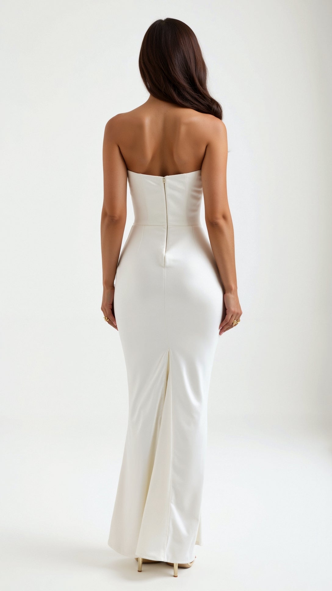 Back view of a woman wearing a white strapless maxi dress, showcasing the sleek, fitted silhouette and a small back slit detail.
