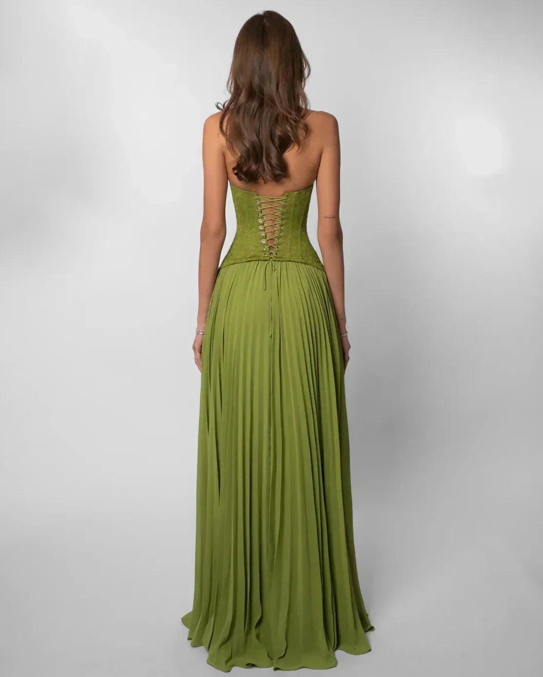 Back view of green lace maxi dress showing corset detail on bodice and pleated skirt for women.